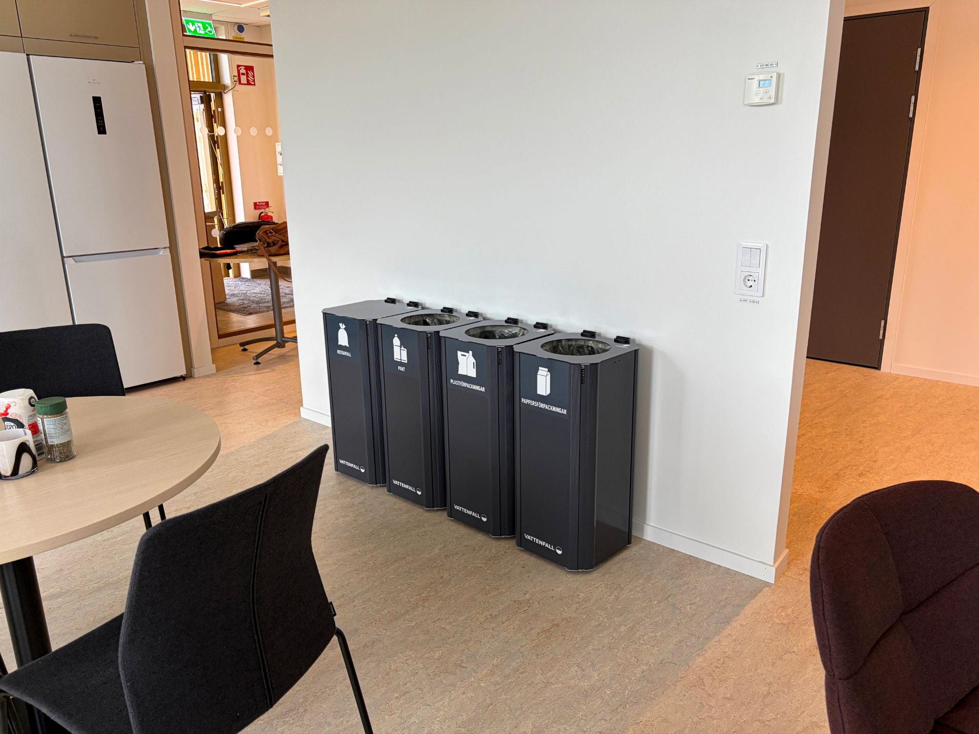 Fyra mörkgrå Kiwi kärl med Vattenfalls märkning för restavfall, pant, plastförpackningar och pappersförpackningar i ett pentry