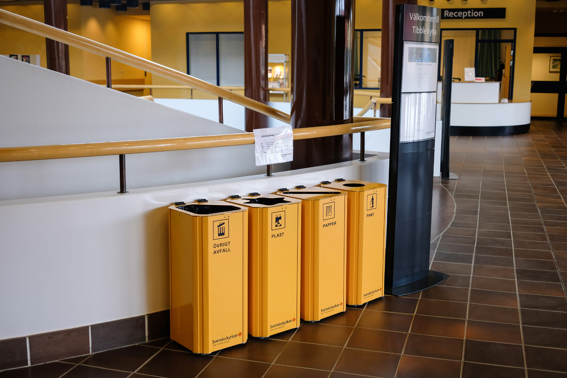 Fyra gula Kiwi kärl för övrigt avfall, plast, papper och pant i entrén till Tibble kyrka