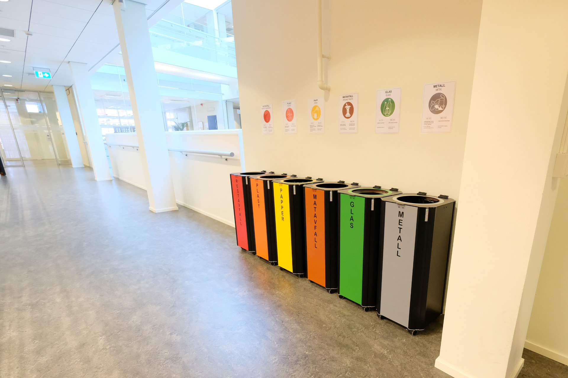 Sex Kiwi kärl med färgade fronter för restavfall, plast, papper, matavfall, glas och metall i en korridor på Göteborgs universitet
