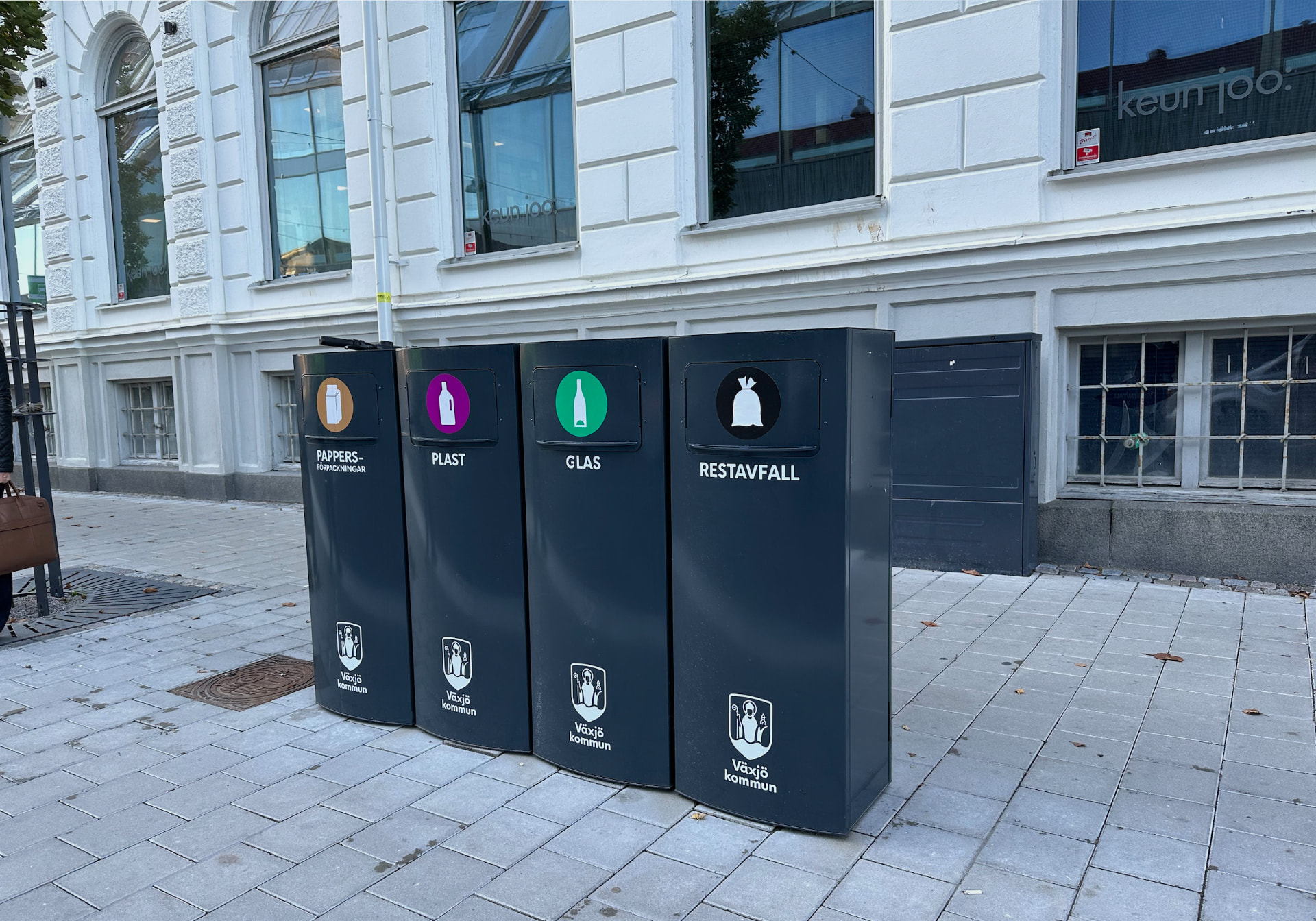 Fyra Sortify Mango kärl med Växjö kommuns märkning för papper, plast, glas och restavfall längs en fasad