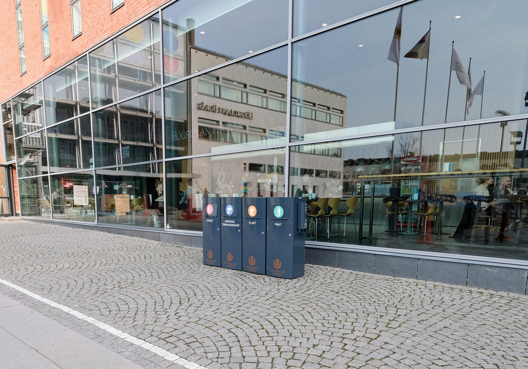 Fyra mörka Mango M-kärl för övrigt, pappersförpackningar, plast och pant utanför Borås Högskola