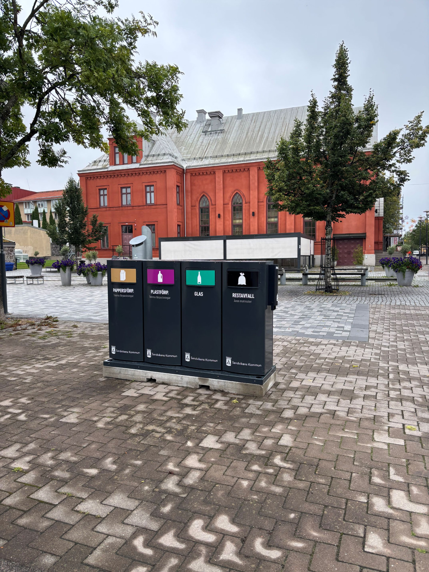 Fyra svarta Sortify Mango kärl med Sandvikens kommuns märkning på ett torg framför en tegelbyggnad