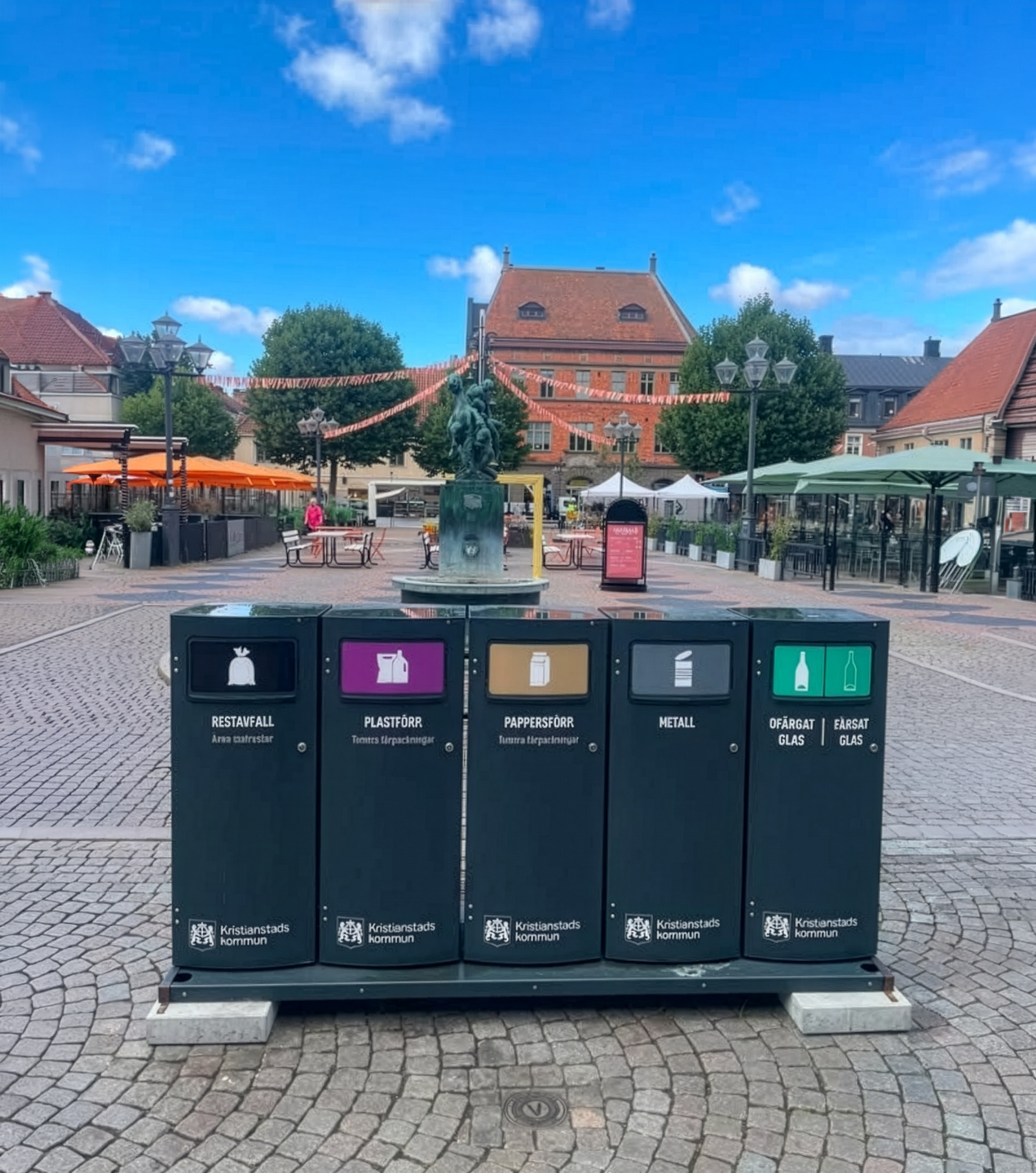 Fem Mango M kärl med Kristianstads kommuns märkning på ett stadstorg