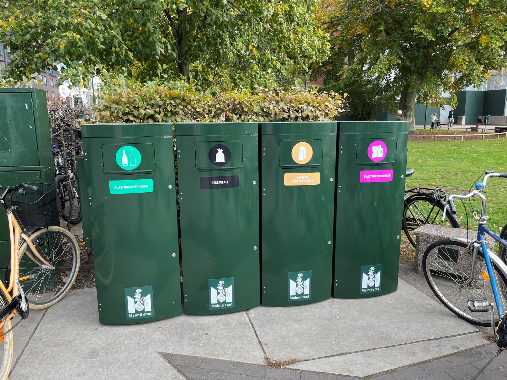 Fyra mörkgröna Mango XL kärl för glasförpackningar, restavfall, pappersförpackningar och plastförpackningar i en park i Malmö